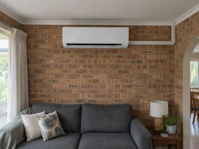 Wall-mounted split system on a brick living room wall above a sofa in a home in Elanora